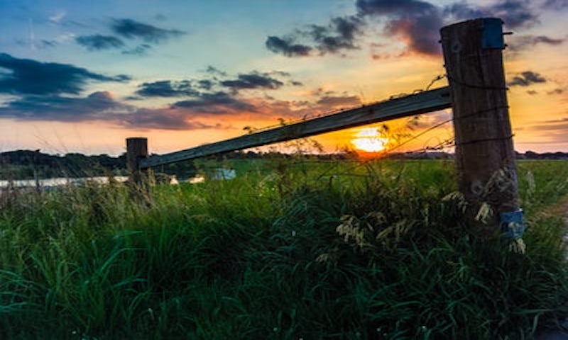 The Flint Hills National Scenic Byway offers incredible views of the native grasses and flowers of the tallgrass prairie. It's one of the last remaining such landscapes left in America. Much of the land along the Byway hasn't changed in thousands of years ago when the Kaw, Osage and other native tribes lived here. The area is part of the famous Santa Fe Trail, creating many prairie towns along the way. Flint Hills National Scenic Byway sunset over wooden post in the flint hills
